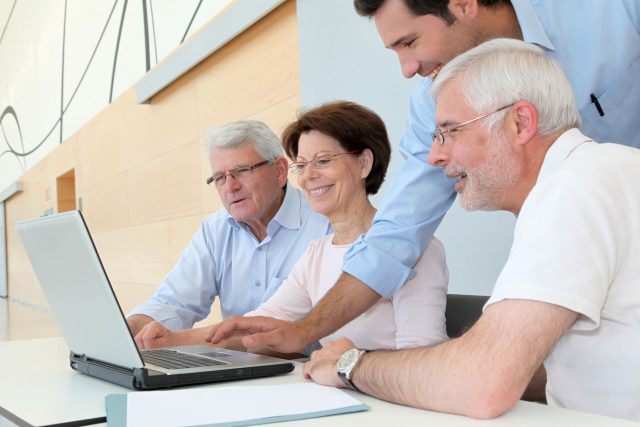 a group of people sitting around a laptop computer.